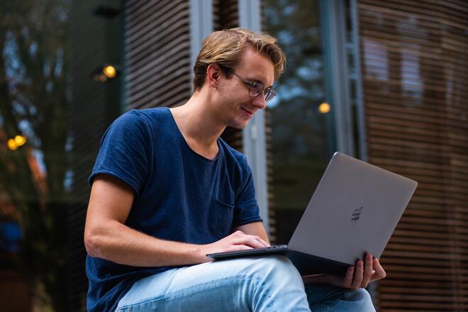 Male student using a laptop on his lap and smiling