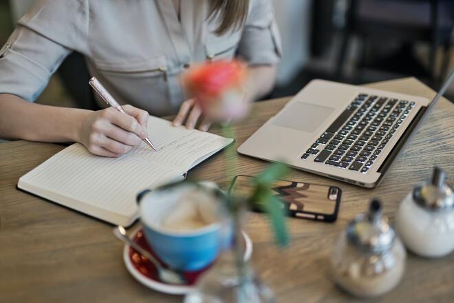 Student writing in a notebook in front of a laptop